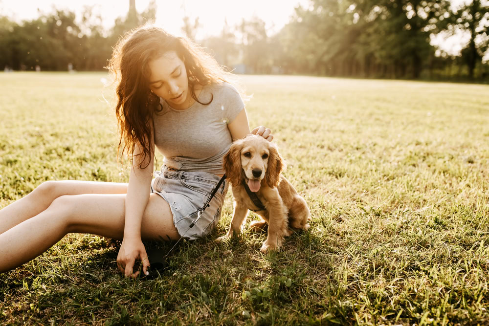 girl-or-woman-sitting-on-a-grass-in-park-with-her-cocker-spaniel-puppy