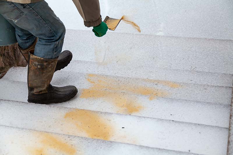 A hand in a green glove sprinkles sand on the icy steps