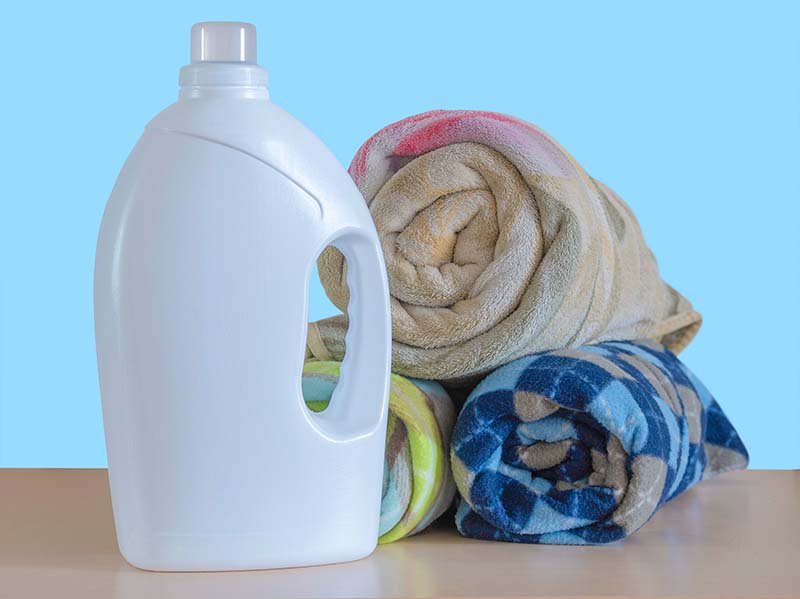 A large white plastic bottle of laundry detergent and a stack of rolled-up blankets