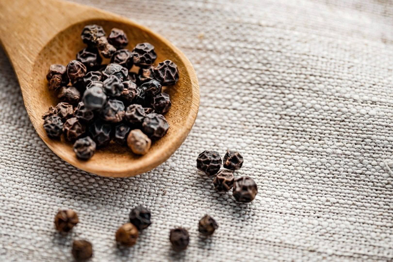 Black peppercorns on wooden spoon