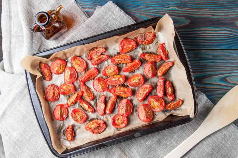 Dried tomatoes in baking tray and spatula on blue wooden background