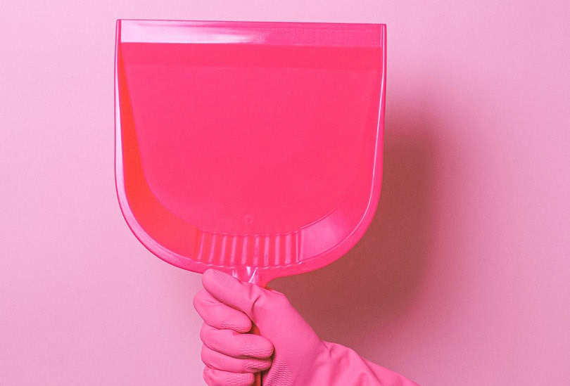 a hand with pink gloves holding up a pink dust pan