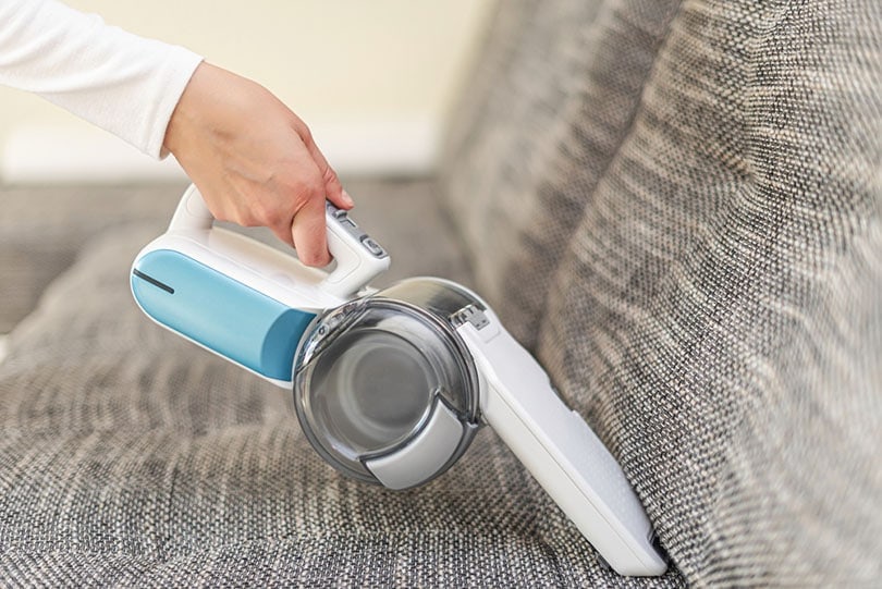 a woman vacuuming furniture in a house with a hand held portable vacuum cleaner