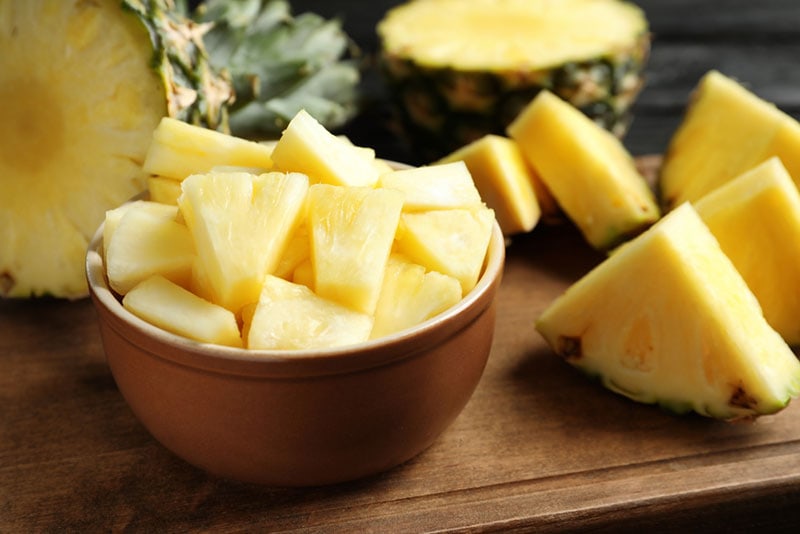 bowl with fresh sliced pineapple on wooden board