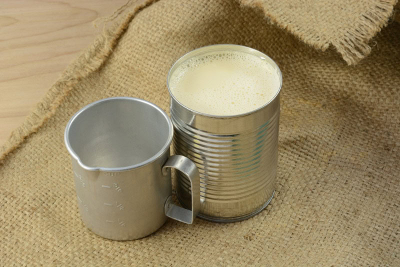 canned evaporated milk and measuring cup on burlap