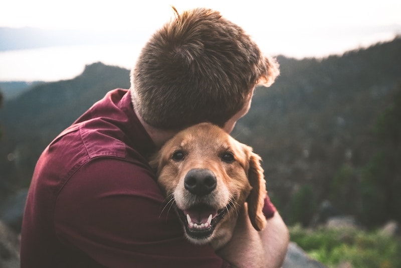 man hugging golden retriever dog outside