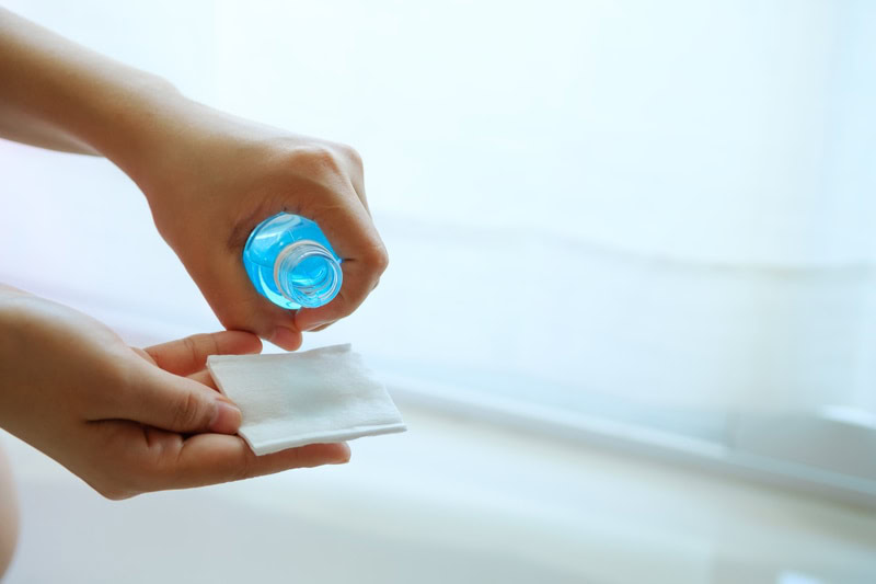 person holding rubbing alcohol and cotton pad