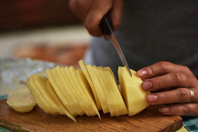 person slicing a potato on the chopping board