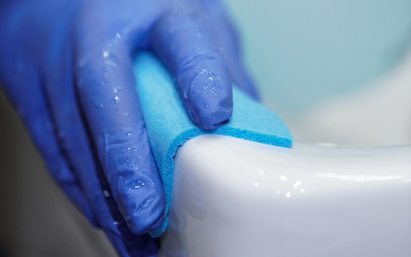 person with gloves cleaning bathroom surface