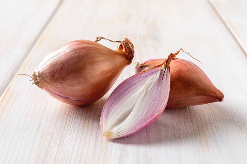 whole and half red eschalots on a white wooden table