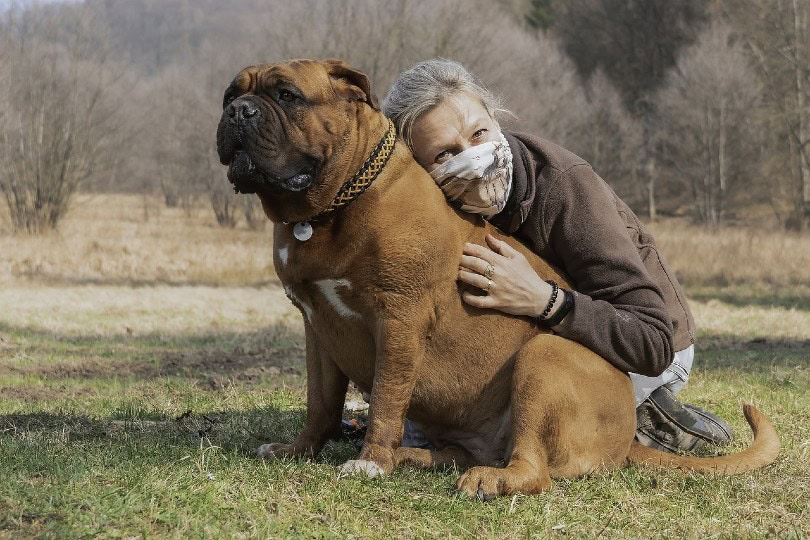 woman hugging her dog while wearing a mask