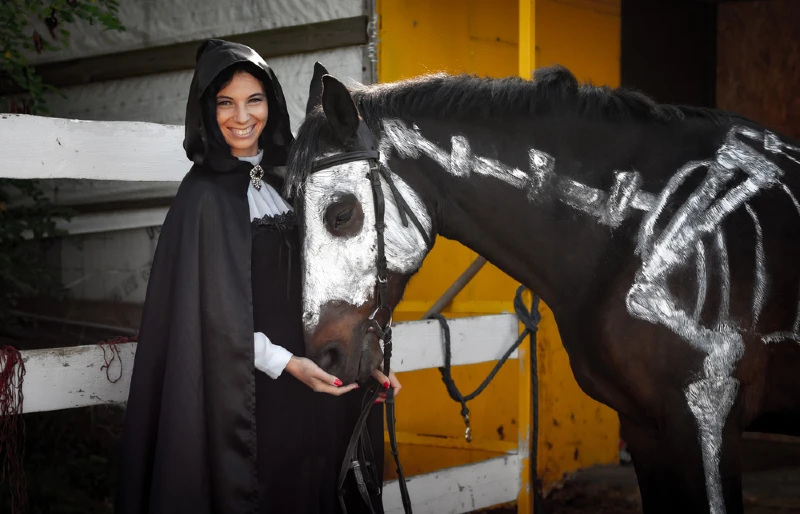 woman in black beside a horse with painted-on skeleton costume