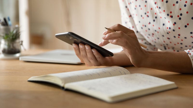 woman making notes on smartphone and in notebook