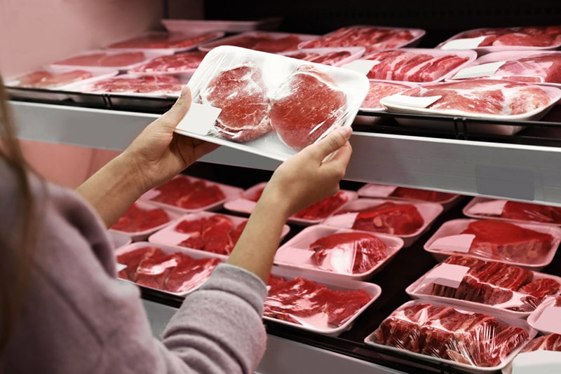 woman taking packed pork meat from shelf